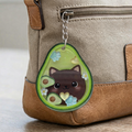 Avocado-shaped keychain with a cat design attached to a beige bag.