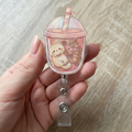 kawaii cat in a bubble tea cup holder held by a hand on a light wooden surface