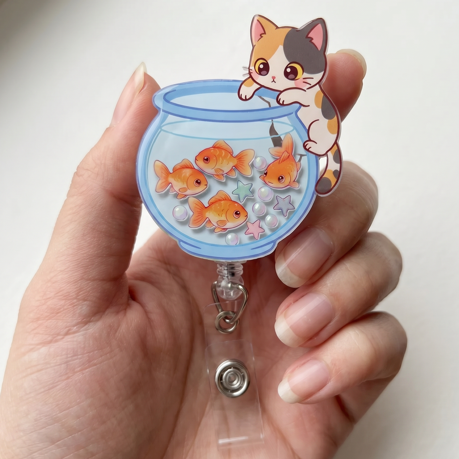 Hand holding a badge reel with a kawaii cat and goldfish design on a white background