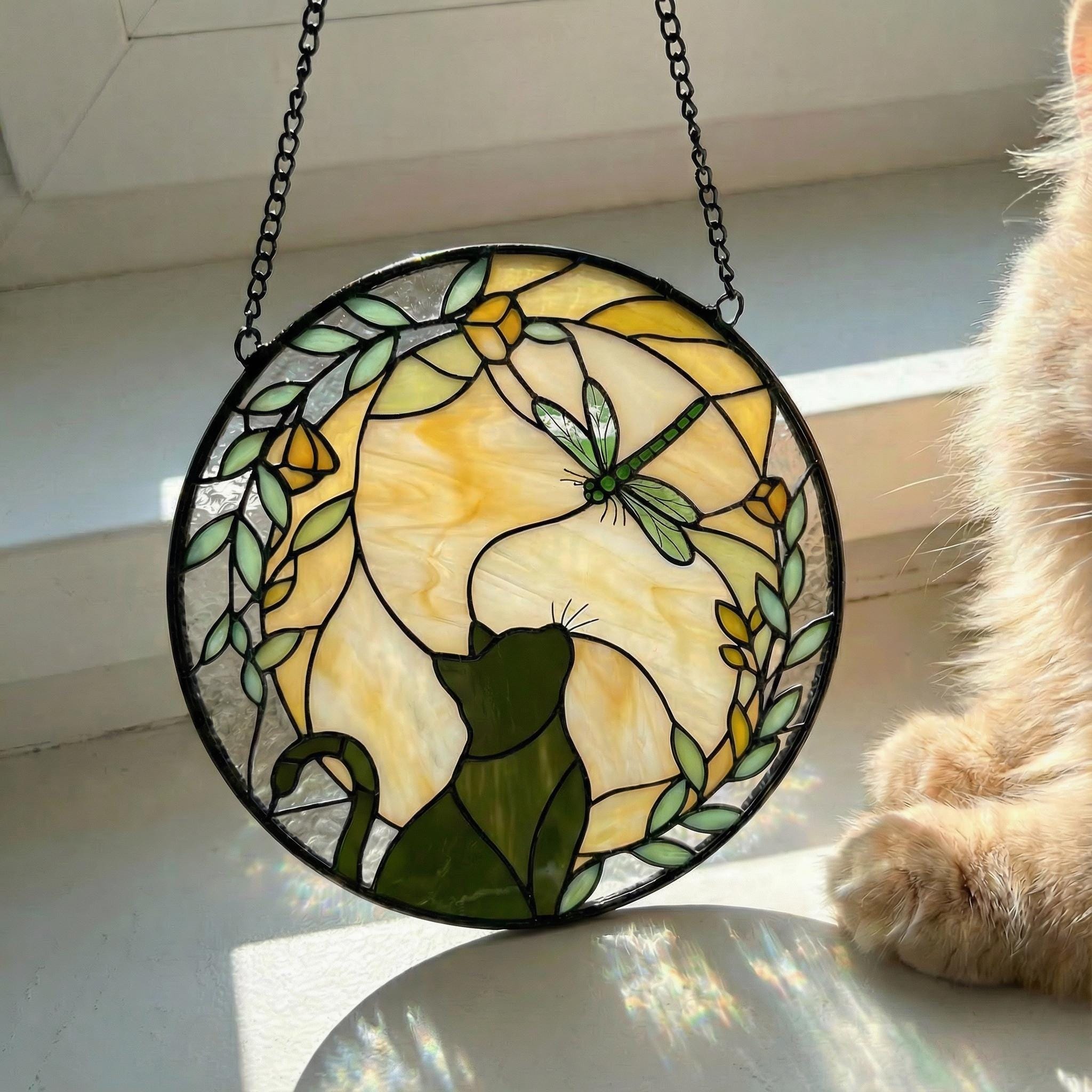 Stained glass panel with a cat and dragonfly design, hanging on a chain.