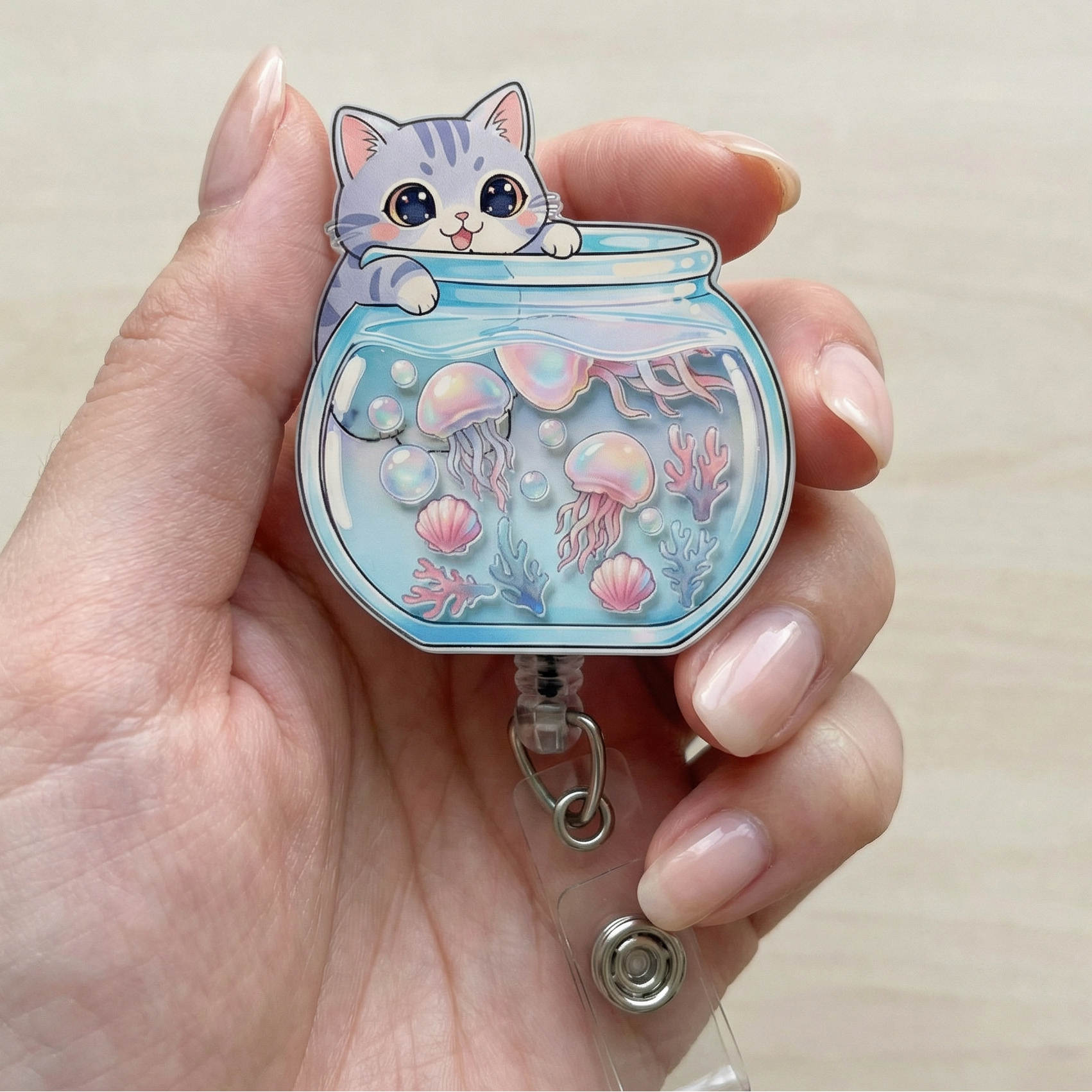 Hand holding a decorative badge holder with a chibi cat in a fishbowl with jellyfish design.