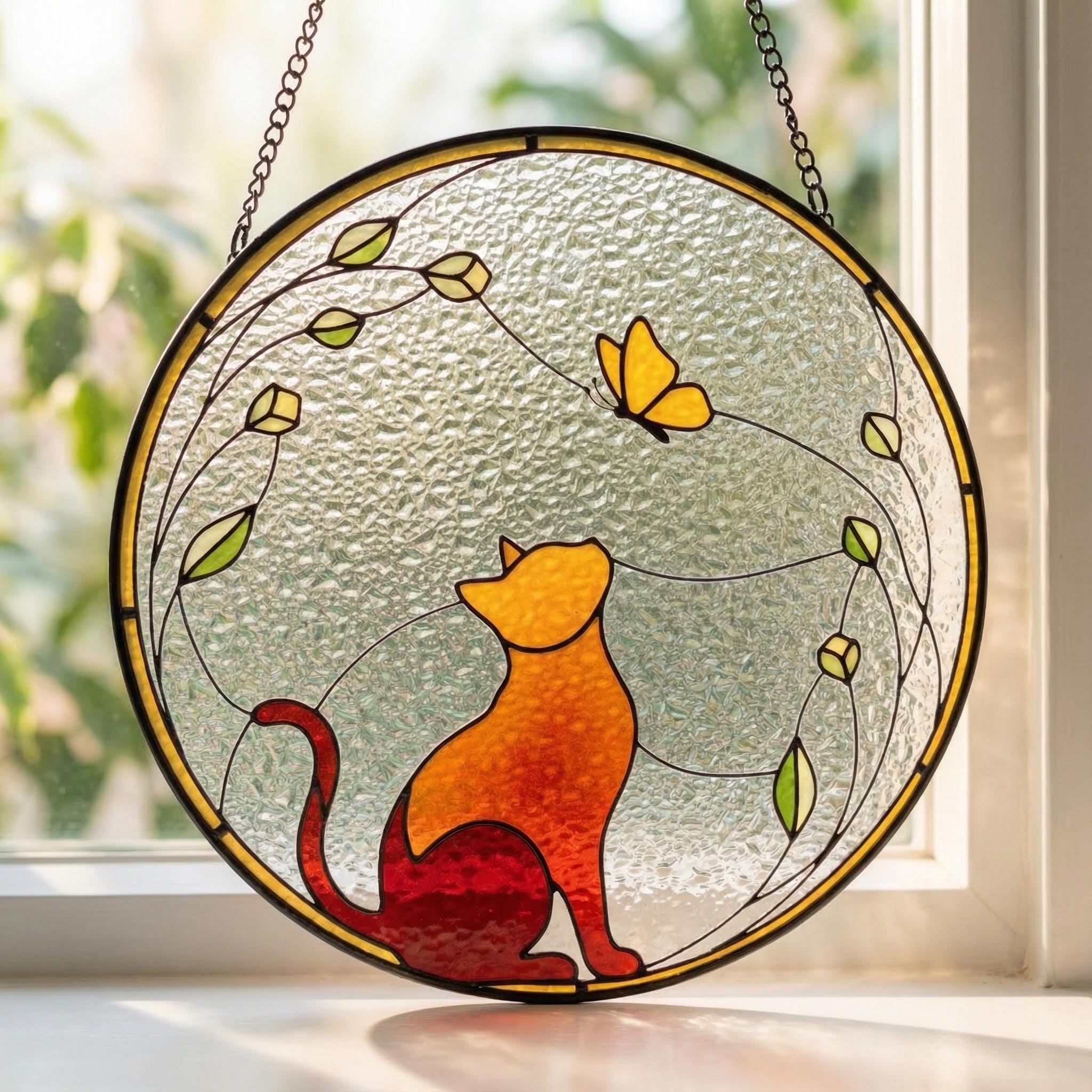 Stained glass panel with a cat and butterfly design on a window sill.