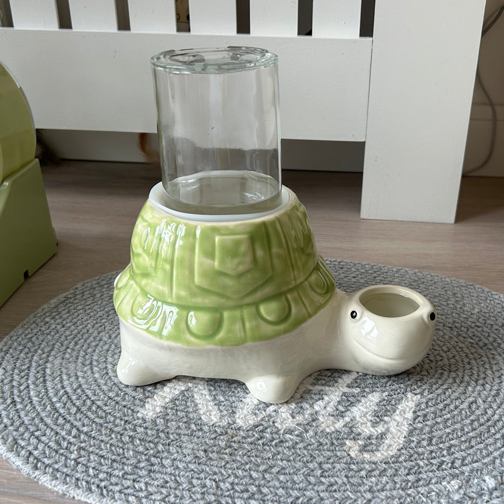 Tortoise turtle-shaped anti gravity water bowl for no wet cat chins with a glass container on a textured rug.