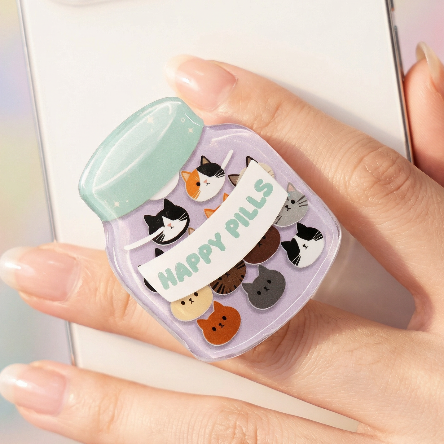 Hand holding a small pill case with cartoon cat designs and 'Happy Pills' text, against a blurred phone background.