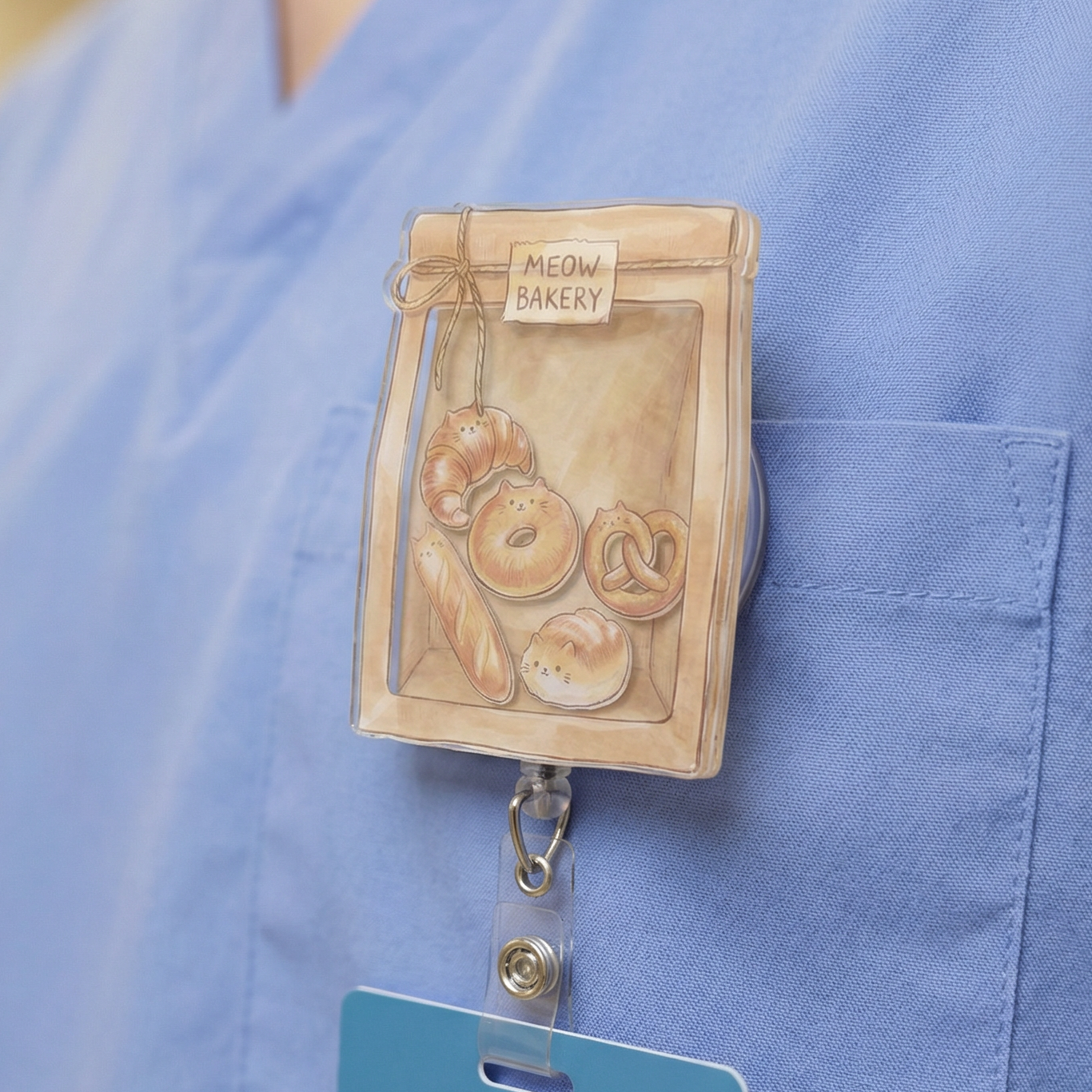 Person wearing a blue scrub top with a meow cat bakery-themed badge holder.