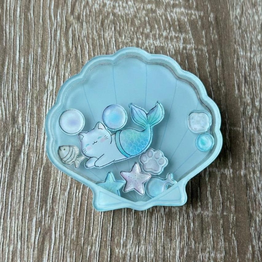 Mermaid cat shaker phone holder inside a shell on a wooden surface