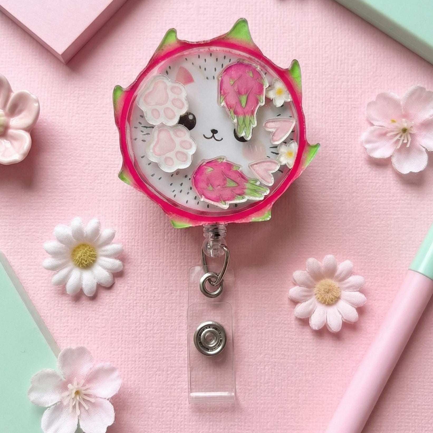 kawaii dragon fruit cat badge holder on a pink background with flowers and stationery items