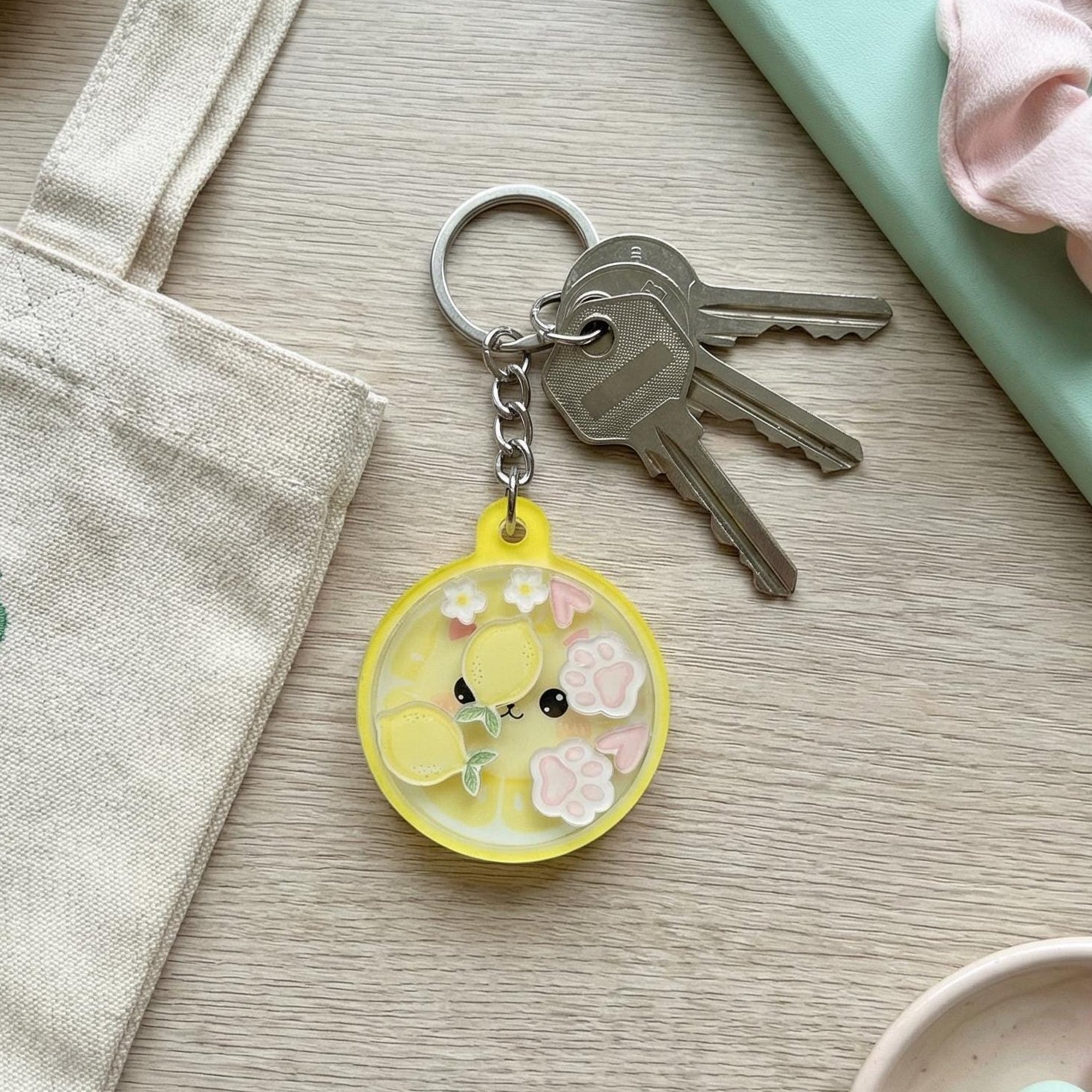 Keychain with a lemon cat design on a wooden surface with a notebook and pastel candies.