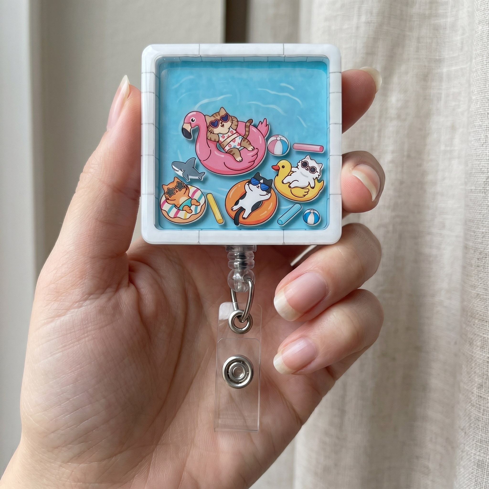 Hand holding a decorative badge holder with kawaii cat pool party designs on a light background