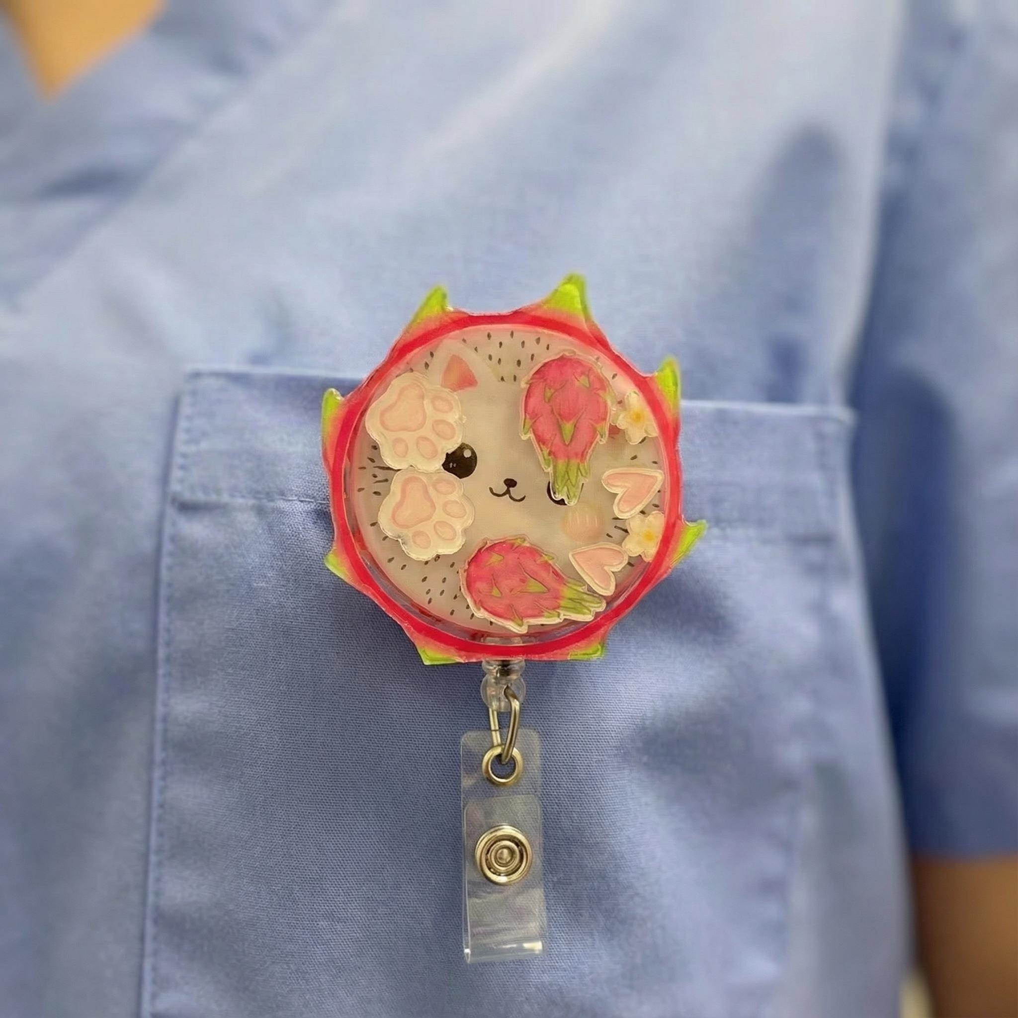 Kawaii-style dragon fruit badge holder with a cat on a blue nurse scrubs