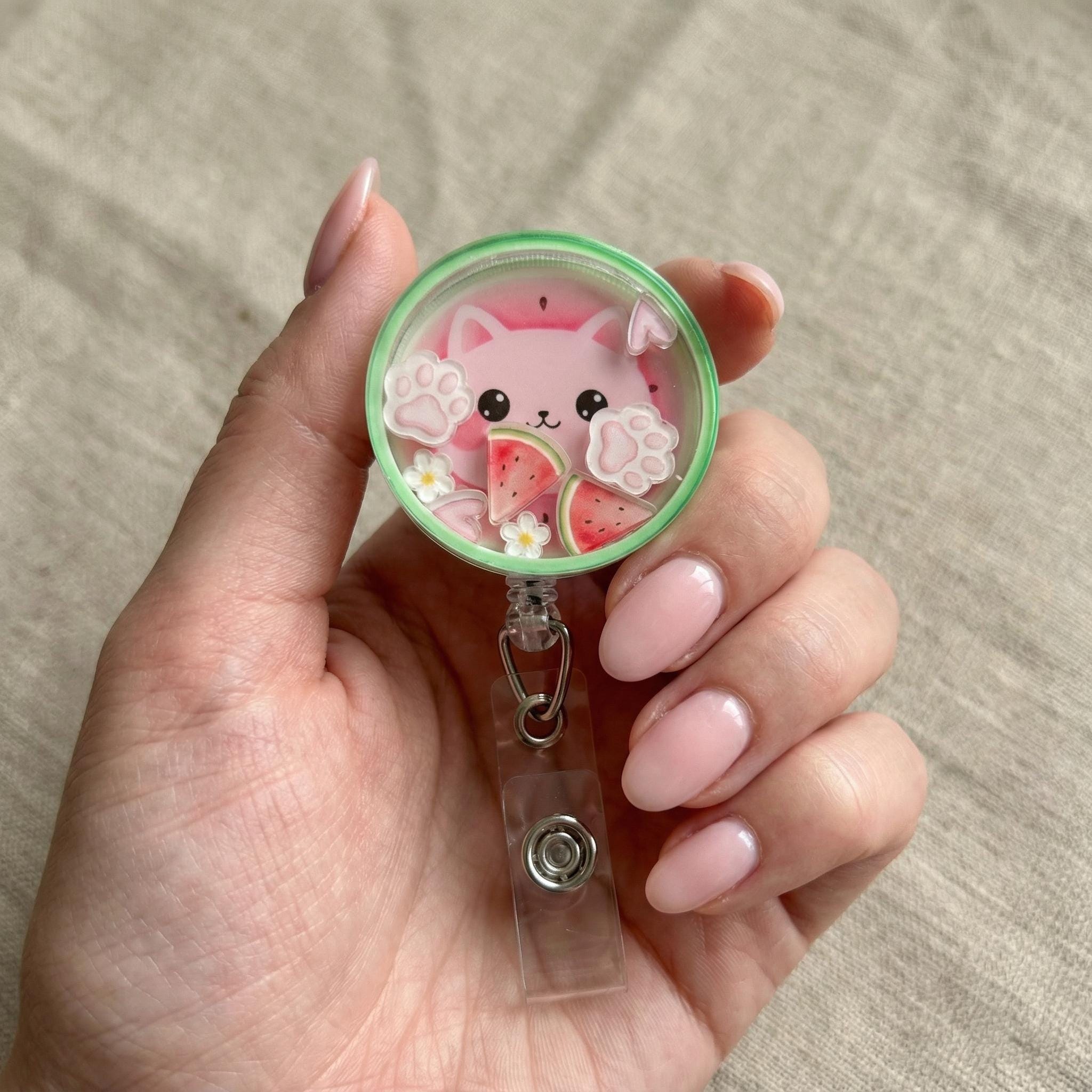 Hand holding a cute pink cat-themed badge holder with watermelon design on a neutral background