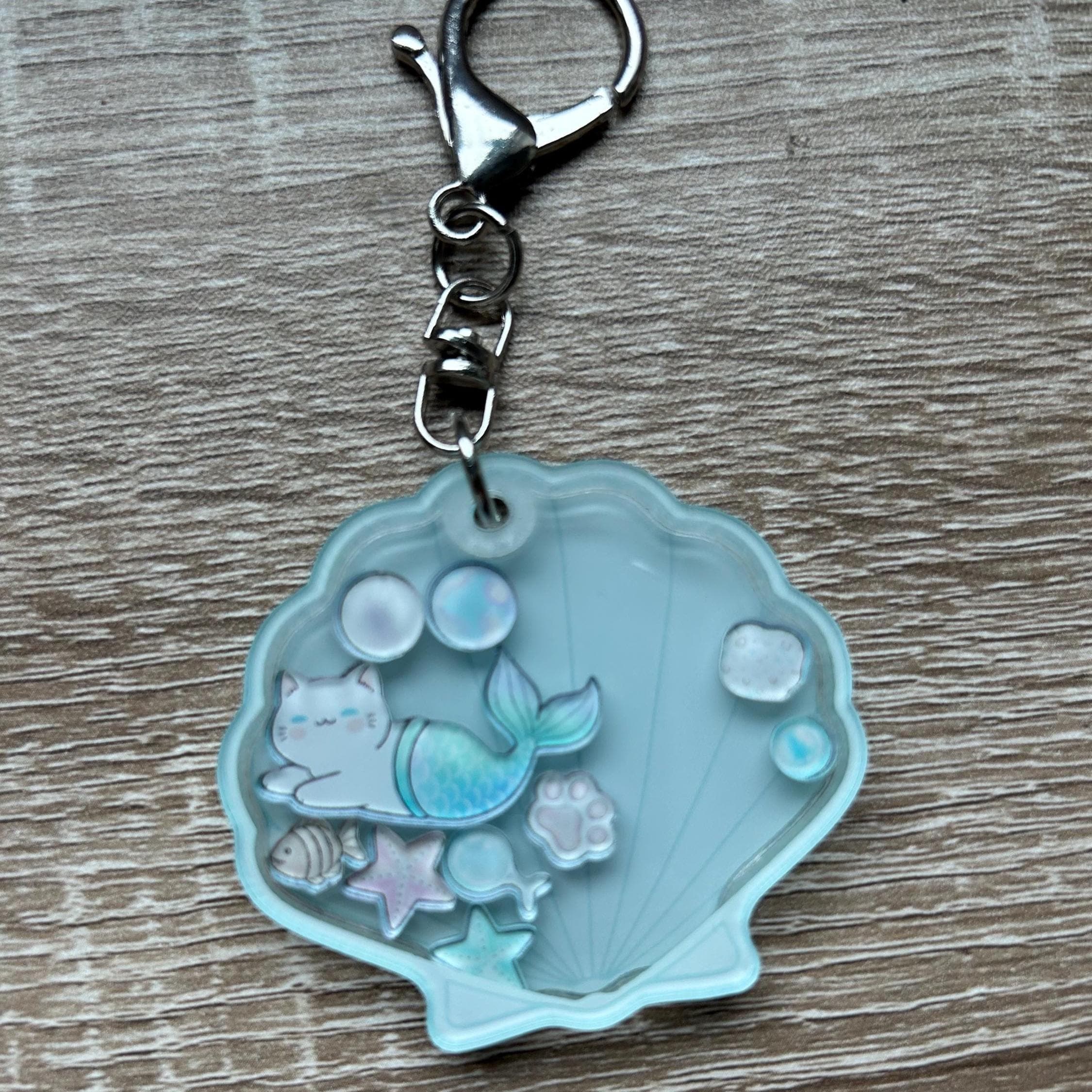 Keychain with a mermaid cat design inside a shell on a wooden surface