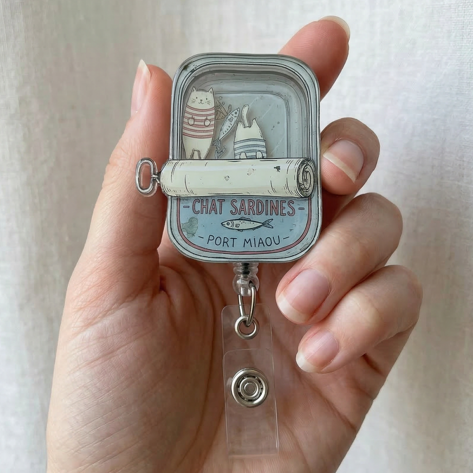 Hand holding a small metal container with french cats in a cartoon sardine tin on a plain background