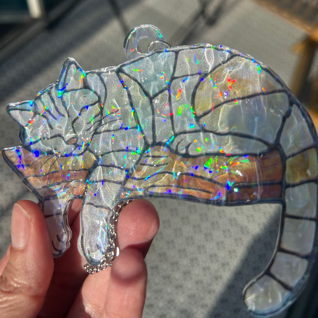 Holographic stained glass cat sleeping on a tree branch sun catcher held by a hand with a blurred background