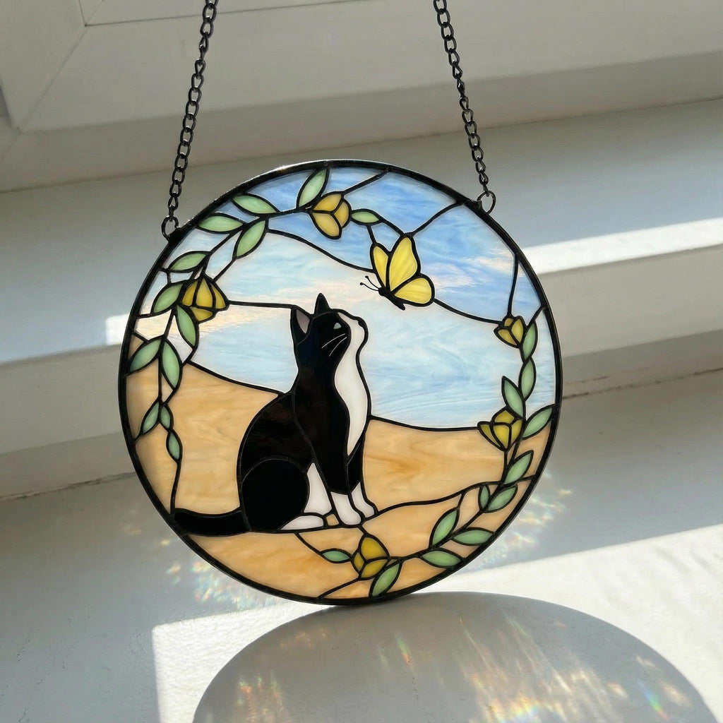 Stained glass sun catcher with a tuxedo cat and yellow butterfly design on a white surface